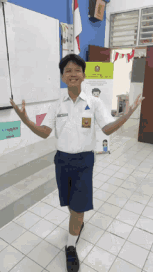 a boy wearing a white shirt and blue shorts stands in a hallway with his arms out