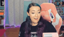 a woman with blue and purple hair is sitting in a pink and white gaming chair .