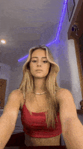 a woman in a red crop top is taking a selfie in a room with purple lights on the ceiling