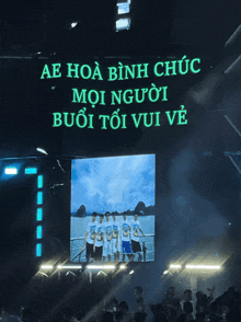 a group of people are standing in front of a screen that says ae hoa bình chuc
