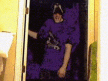 a person is standing in a doorway wearing a purple shirt and a hat .