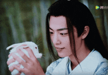 a man with long hair is holding a small white rabbit with chinese writing on the screen behind him