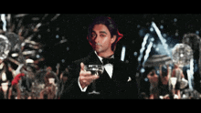 a man in a tuxedo holds a glass of wine