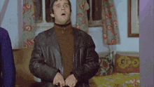 a man in a leather jacket is standing in a bedroom