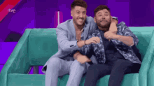 two men are sitting on a couch with a purple background and the word rtve on the bottom right