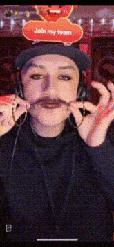 a woman wearing a hat and headphones holds a fake mustache in front of a join my team sign