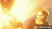 a woman is standing in front of a fireball and a make a gif.com logo