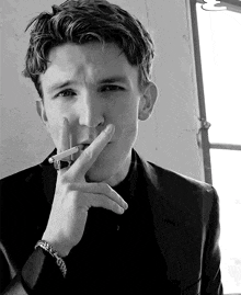 a man in a suit is smoking a cigarette in front of a window .