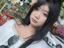 a woman wearing sunglasses looks at the camera with a white car in the background