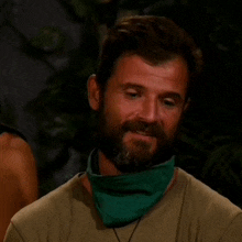 a man with a beard and a green scarf around his neck is looking down .