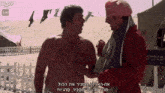 two men are talking on a beach with a sign that says 1:00 in the background