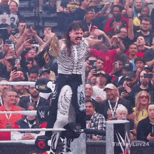 a man in a skeleton costume holds a wrestling trophy in front of a crowd that is taking pictures