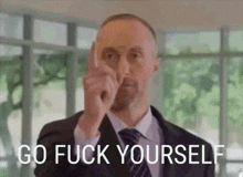 a man in a suit and tie is pointing at the camera with the words go fuck yourself above him