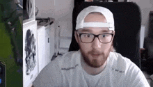 a man with a beard and glasses is wearing a white hat and a white shirt .