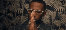 a man wearing sunglasses and a necklace is sitting in front of a palm tree wallpaper