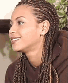 a woman with braids in her hair is smiling and wearing earrings .