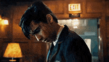 a man in a suit with blood on his face is standing in front of an exit sign in a room .