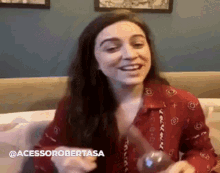 a woman in a red shirt is sitting on a couch smiling and holding a glass .
