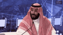 a man in a keffiyeh is sitting at a table with a microphone in front of him .
