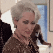 a woman with gray hair is wearing a gold jacket and a necklace