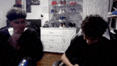 two boys are sitting in front of a microphone in a room with a dresser full of shoes