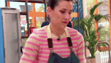 a woman wearing a pink and white striped sweater and apron is standing in front of a window with rtve written on it