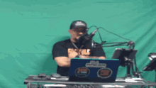 a man sitting in front of a microphone with a laptop that says gm racer on it