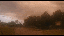 a cloudy sky with a few trees in the foreground and a few houses in the background