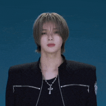 a young man wearing a black jacket and a cross necklace is looking at the camera .