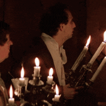 a man with a cigarette in his mouth sits in front of a candle holder