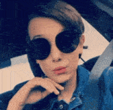 a young girl wearing sunglasses and a denim jacket is sitting in a car