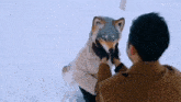 a man is holding a stuffed animal that looks like a wolf in the snow .