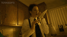 a man in a white shirt and black tie is holding a knife in his hand in a kitchen with the words terasgifs below him