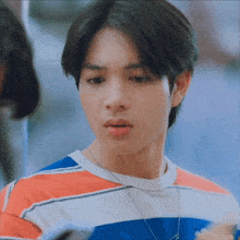 a young man wearing a striped shirt and a necklace is looking at something
