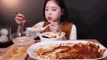 a woman is sitting at a table eating a plate of food with chopsticks .