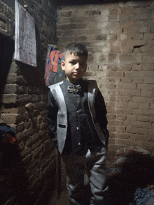 a young boy stands in front of a brick wall