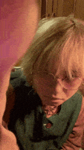 a person with blonde hair and glasses is wearing a green shirt