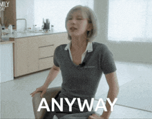a woman in a grey shirt is sitting in front of a kitchen and the word anyway is visible