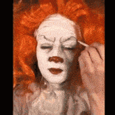 a person is applying makeup to a clown with orange hair