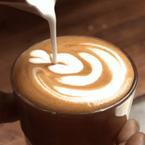 Latte art, pouring steamed milk into coffee, creating a flower and leaves