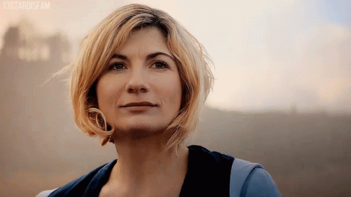 The thirteenth Doctor, played by Jodie Whittaker, smiles at the camera in a dusty environment.