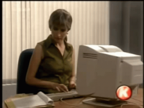 Gif: woman in a office, at an 90s style PC, sweeps the monitor off the desk, keeps typing
