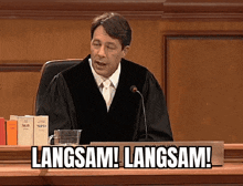 a man in a judge 's robe is sitting at a desk with a sign that says langsam langsam