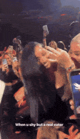 a woman taking a picture of another woman in a crowd with the caption when u shy but a real eater