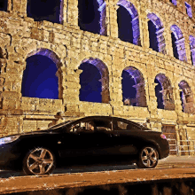 a black car is parked in front of a building with arches