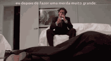 a man in a suit is sitting on a couch and smoking a cigarette with a caption that says eu depois