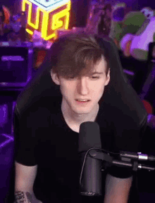 a young man is sitting in a chair in front of a microphone and looking at the camera .