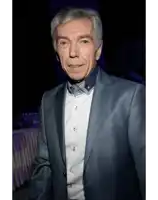 a man in a suit and white shirt stands in front of a table