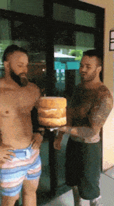 a shirtless man is holding a stack of cakes in front of another shirtless man