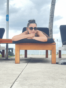 a woman wearing sunglasses is laying on a wooden lounge chair